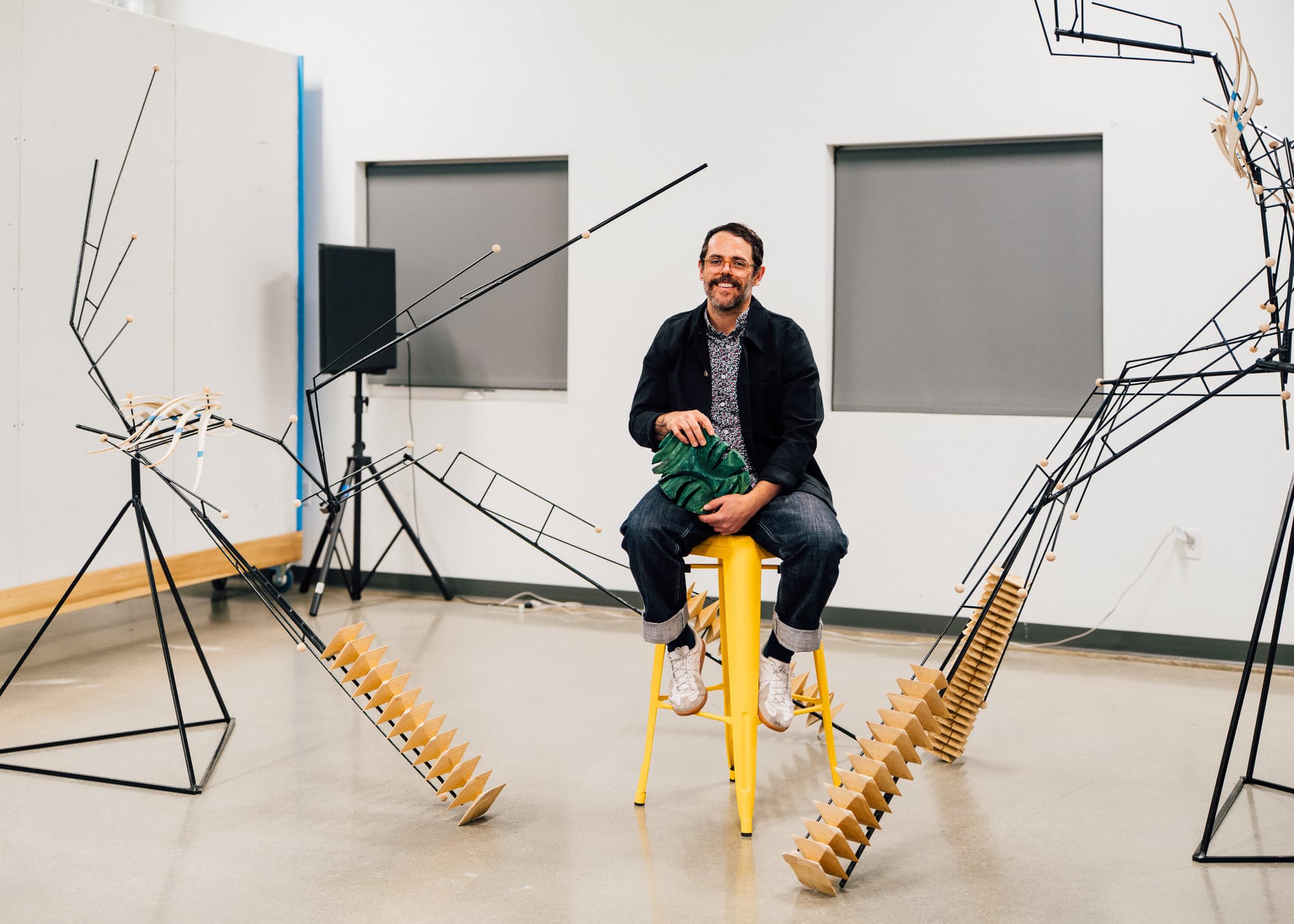 A man sits on a stool surrounded by figural metal sculptures.