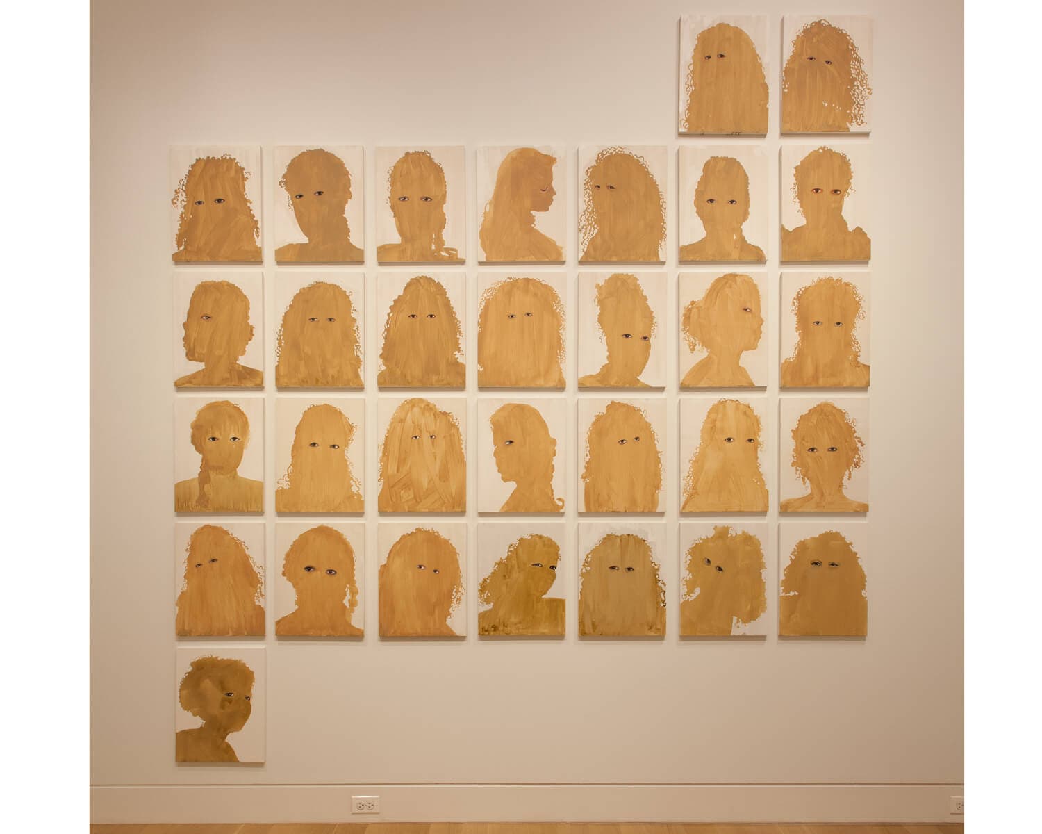 Faces made of paper bags arranged in a grid on a gallery wall.
