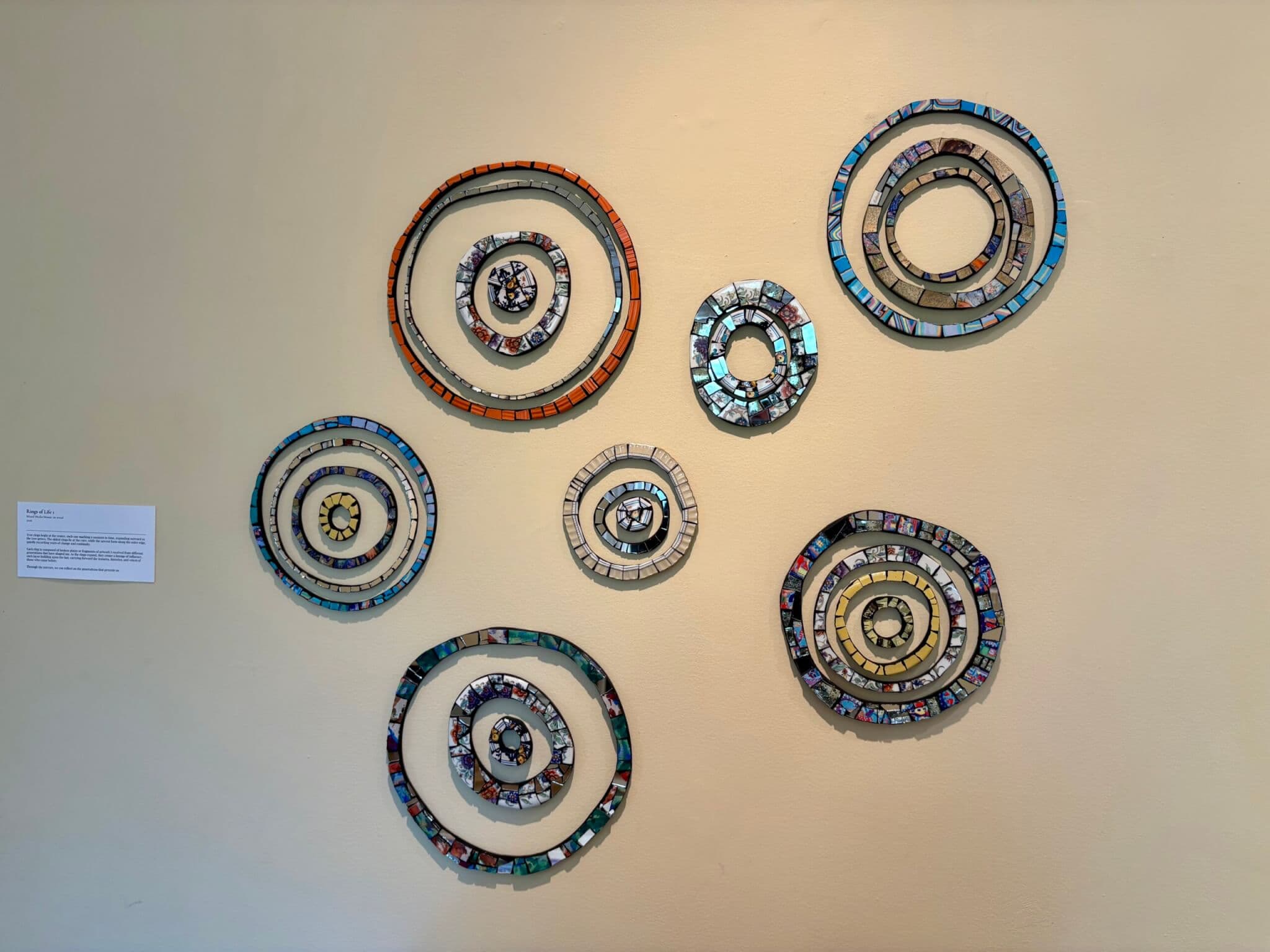 Multiple circular mosaic artworks hang on a gallery wall.