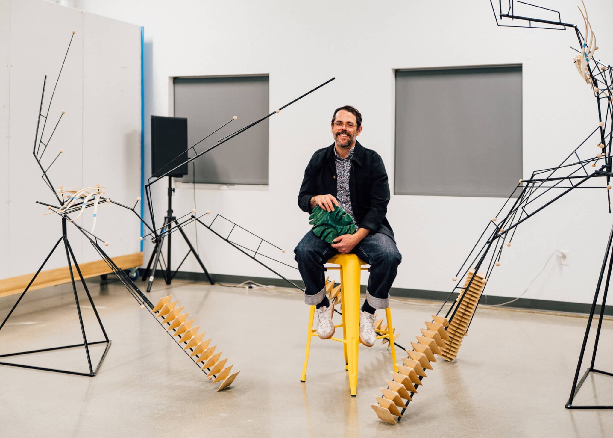 A man sits on a stool surrounded by figural metal sculptures.